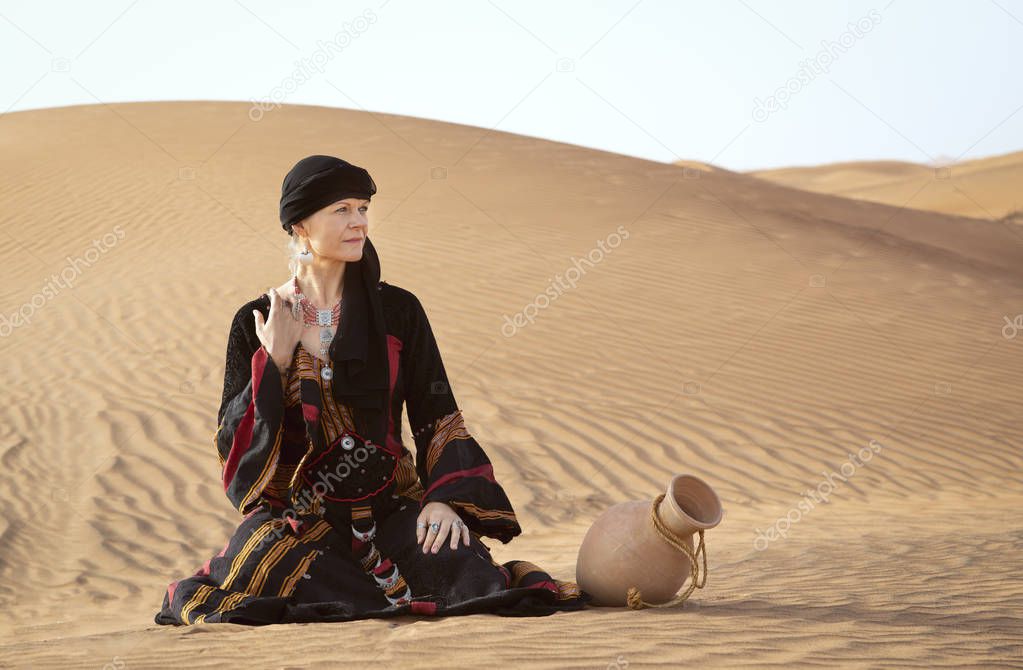 middle aged woman in yemeni traditional dress in desert with water dish