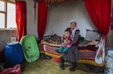 Bayan Olgii, Moğolistan - 29 Eylül 2015: Moğol kazak göçebe granmother bir çocuk onun kucağına bir kış evin içinde tutan