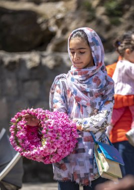 Niasar, Iran - 25th April, 2019: Iranian young girl with flowers, selling them to passersby during rose picking season clipart