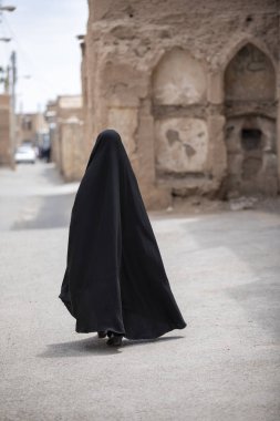 İranlı bayan arka görünümü, tamamen onu siyah burka İran'da eski köyün sokaklarında yürüyüş kaplı