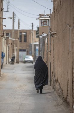İranlı bayan arka görünümü, tamamen onu siyah burka İran'da eski köyün sokaklarında yürüyüş kaplı