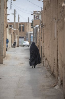 İranlı bayan arka görünümü, tamamen onu siyah burka İran'da eski köyün sokaklarında yürüyüş kaplı