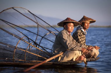 Göl, Inle, Myanmar, 17 Kasım 2014: Inle Gölü balıkçıları günün erken saatlerinde sörf sırasında teknede sigara içiyorlar.