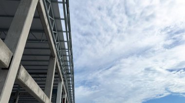 Bulutlu gökyüzü arka planına sahip beton ve çelik bina yapısı, modern endüstriyel mimari konsepti.