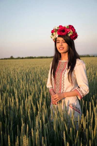 Indian woman in Ukrainian embroidery posing in fieldBeautiful indian young woman in traditional Ukrainian embroidery clothes and floral handmade wreath stand in field, dreaming or thinking, pretty ethnic woman posing in nature