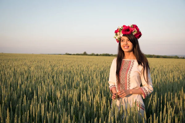 Indian woman in Ukrainian embroidery posing in fieldBeautiful indian young woman in traditional Ukrainian embroidery clothes and floral handmade wreath stand in field, look in distance dreaming or thinking, pretty ethnic woman posing in nature