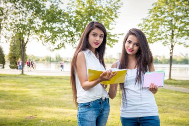 Güzel Hintli kızlar parkta ellerinde defterler ya da kitaplarla iletişim kurarlar. Açık havada iki kız öğrencinin portresi. İki kız da kameraya bakıyor.