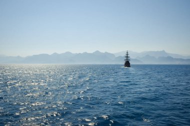 Gemi denizde yelken açıyor. Antalya kıyısı, Türkiye. Mavi gökyüzü ve dağların arka planında. Antalya yakınlarındaki deniz manzarası