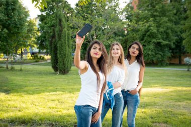 Üç etnik çeşitlilikte kız parkta selfie çekiyor. Genç ve gülümseyen kızlar. Çalışmaktan ya da işten boş zaman