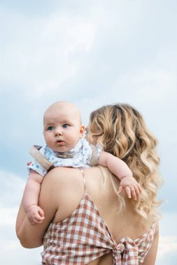 Sarışın anne oğlunu omzunda taşıyor. Çocuk merakla etrafına bakıyor. Büyük mavi ya da koyu mavi gözlü küçük oğlan. Fotoğrafın doğal renkleri.