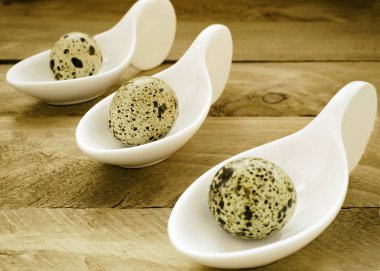 Ahşap arka plan ve Tarih yerleştirilmiş üç beyaz kaşık ile üç bıldırcın yumurtası