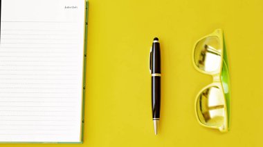 Defter, kalem ve sarı gözlük, sarı bir arka plan üzerinde tüm görücü usulü.