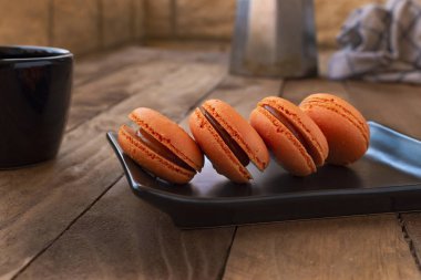 Vintage tarzı ile bir kahve kabı ile ahşap bir masa üzerinde turuncu macarons.