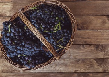 Hasır sepet dolu bir rustik çam ahşap masa üzerinde şarap üzüm.