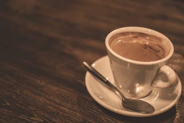 White cup of freshly made coffee on a wooden rustic table.