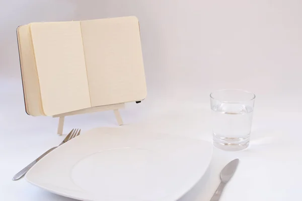 ダイエットのコンセプトです プレート カトラリー 水のガラスのテーブルの上のノートブックを開く白の背景に — ストック写真