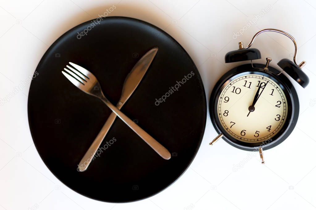 Time concept of dieting. Black alarm clock on a plate with a meal service.