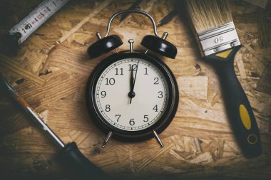 DIY zaman kavramı. Ahşap çalışma masa üzerinde siyah bir çalar saat çevreleyen araçları.