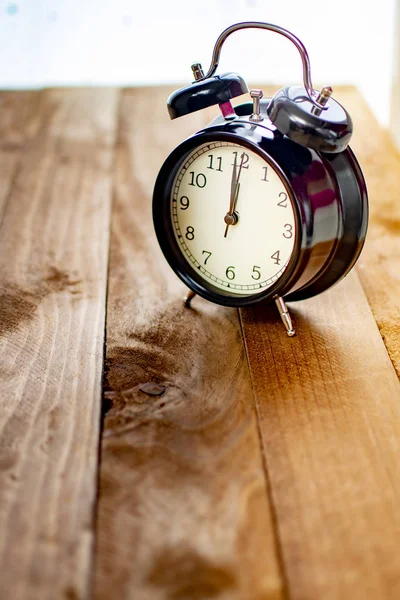 Black alarm clock on old wood, marking twelve o\'clock.