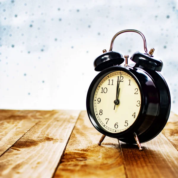 Black alarm clock on old wood, with star background.