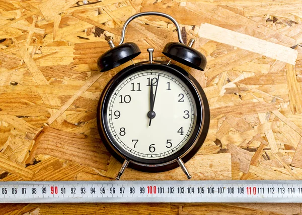 Black alarm clock marking twelve o'clock, on OSB wood.