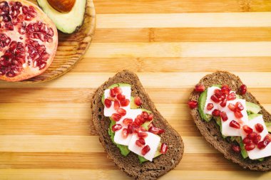 Avokado, kiraz domates ve ahşap üzerine nar tohumları ekmek dilimi.