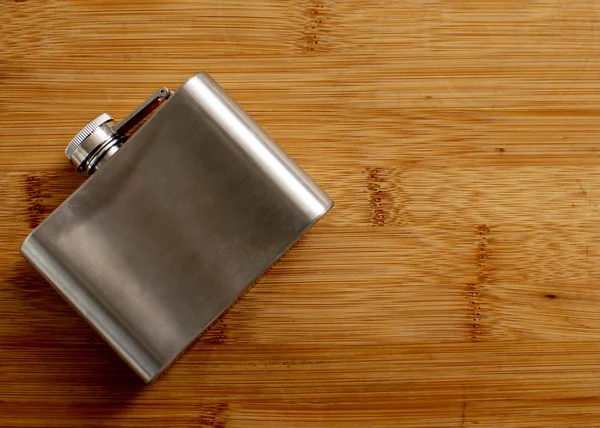 Liquor flask made of metal on a wooden background.