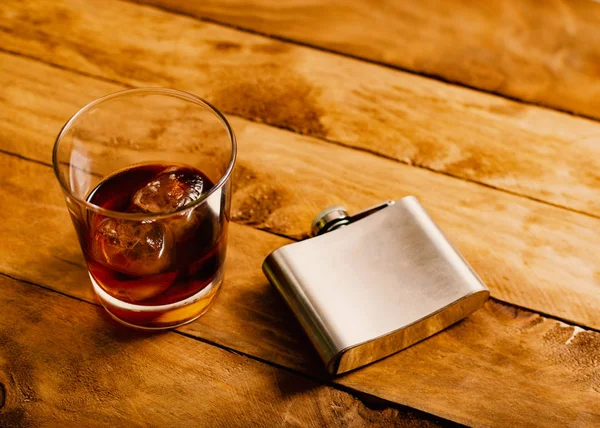 Alkolizm kavramı. Cam bardak viski ve buz yanında bir likör şişesi ile.