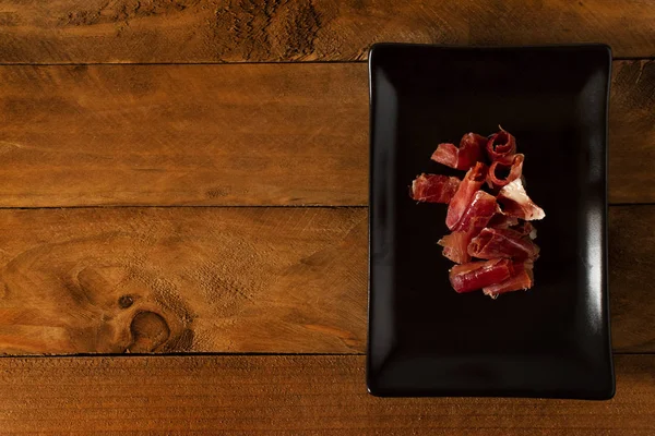 Serrano ham chips on a plate over old wood.