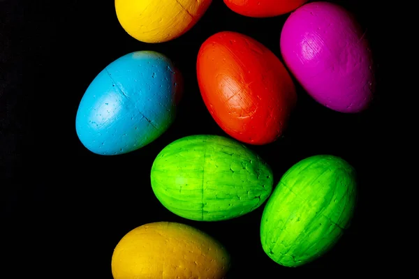 Easter eggs of blue, yellow, orange and green color, on a black background.