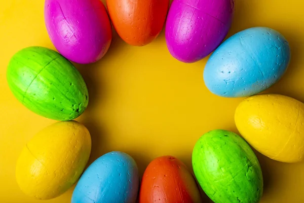 Easter eggs of blue, yellow, orange and green color, on a yellow background.