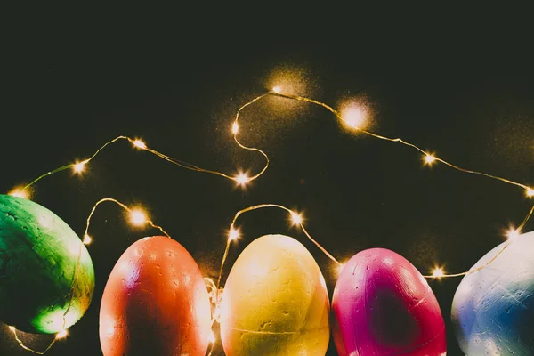 Easter eggs of blue, yellow, orange and green color, on a black background and lights.