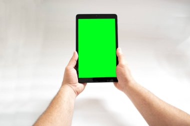 Beyaz arka plan üzerinde iki el ile bağlanmış yeşil ekranlı tablet.