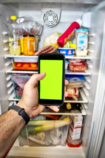 Phone with green screen with the bottom of a refrigerator.