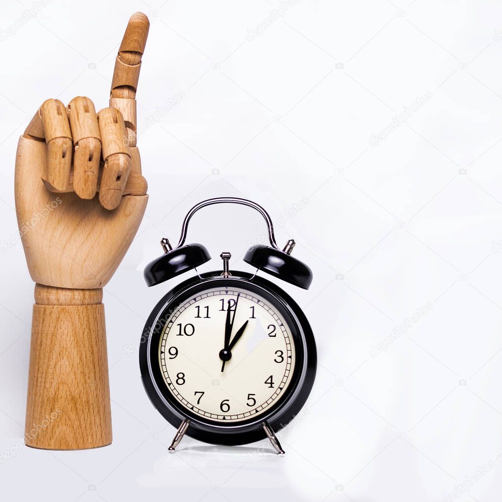 Wooden hand raising a finger, next to a clock