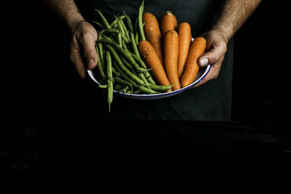 Hombre con delantal verde presentando verduras y verduras de jardín . — Foto de Stock