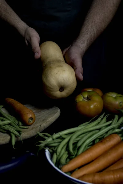 Человек в зеленом фартуке представляет овощи и овощи в саду . — стоковое фото
