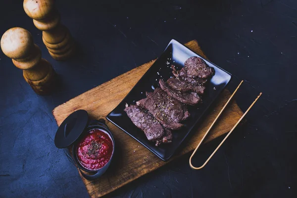 Carne de res cortada en tiras con salsa de tomate sobre madera . — Foto de Stock