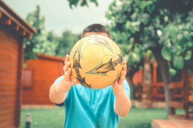 Bahçeli bir kamp alanında elinde futbol topu tutan bir çocuk..