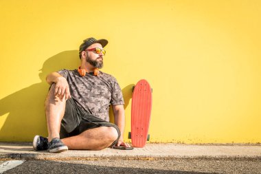 Kaykaylı ve sarı arka planlı kıvrımlı bir adam bekliyor..