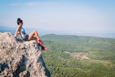 Kadın koşucu dağlara bakarak bir kaya yığınına tırmanıyor..