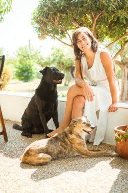 Beyaz elbiseli, rastalı ve köpekleriyle oynayan bir kızın portresi..