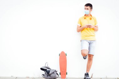 Sarı gömlekli, kaykaylı ve sırt çantalı bir genç duvarda bekliyor..