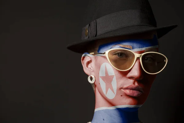 Portrait of woman with painted North Korea flag and sunglasses on black background