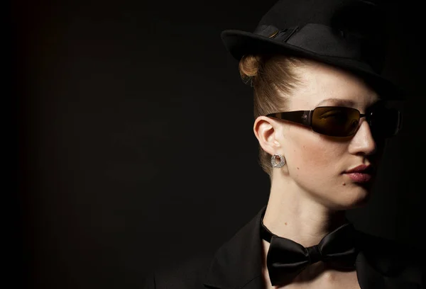 Portrait of woman with bow tie,hat and sunglasses on black
