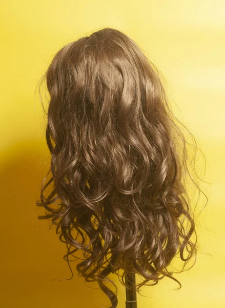 黄色の背景に女性長い巻き毛のかつら — ストック写真
