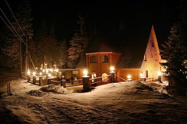 Aralık 2006 'da Ukrayna' nın Dragobrat bölgesindeki Carpathian Dağları 'ndaki rahat ahşap otel. Sıcak ışıklar, kar ve şenlikli atmosferli bir kış gecesi sahnesi..