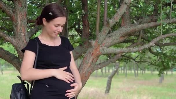 一个年轻的, 美丽的, 怀孕的女孩, 靠近一棵树, 穿着黑色 t恤. — 图库视频影像