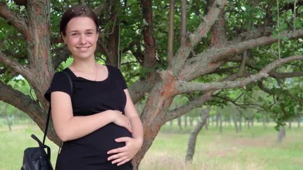 A young, beautiful, pregnant girl, near a tree, in a black T-shirt. — Stock Video