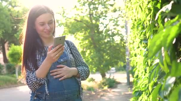녹색 배경에 전화 보고 바지를 입은 소녀가 임신. — 비디오